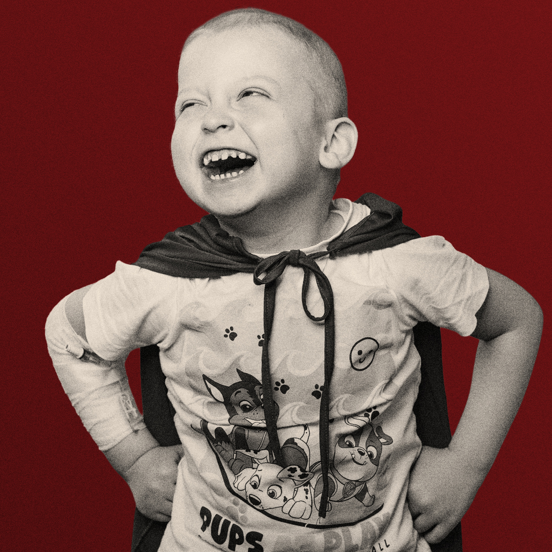 Laughing child wearing a cape against a red background
