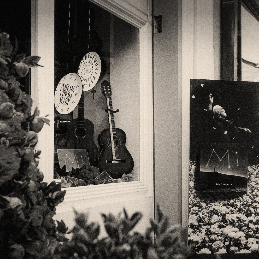 Black-and-white shop window photograph with guitars and a Dino Merlin poster