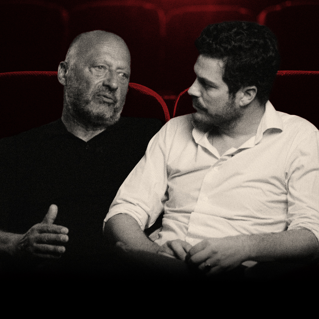 Two men in conversation in red cinema seats